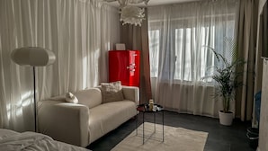 A modern living room with a sofa, a small table, a floor lamp, a red cabinet, and a potted plant.