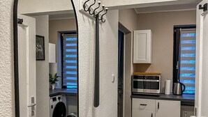 A compact kitchen with a microwave, oven, and coffee maker. A large mirror and a coat rack are mounted on the wall.