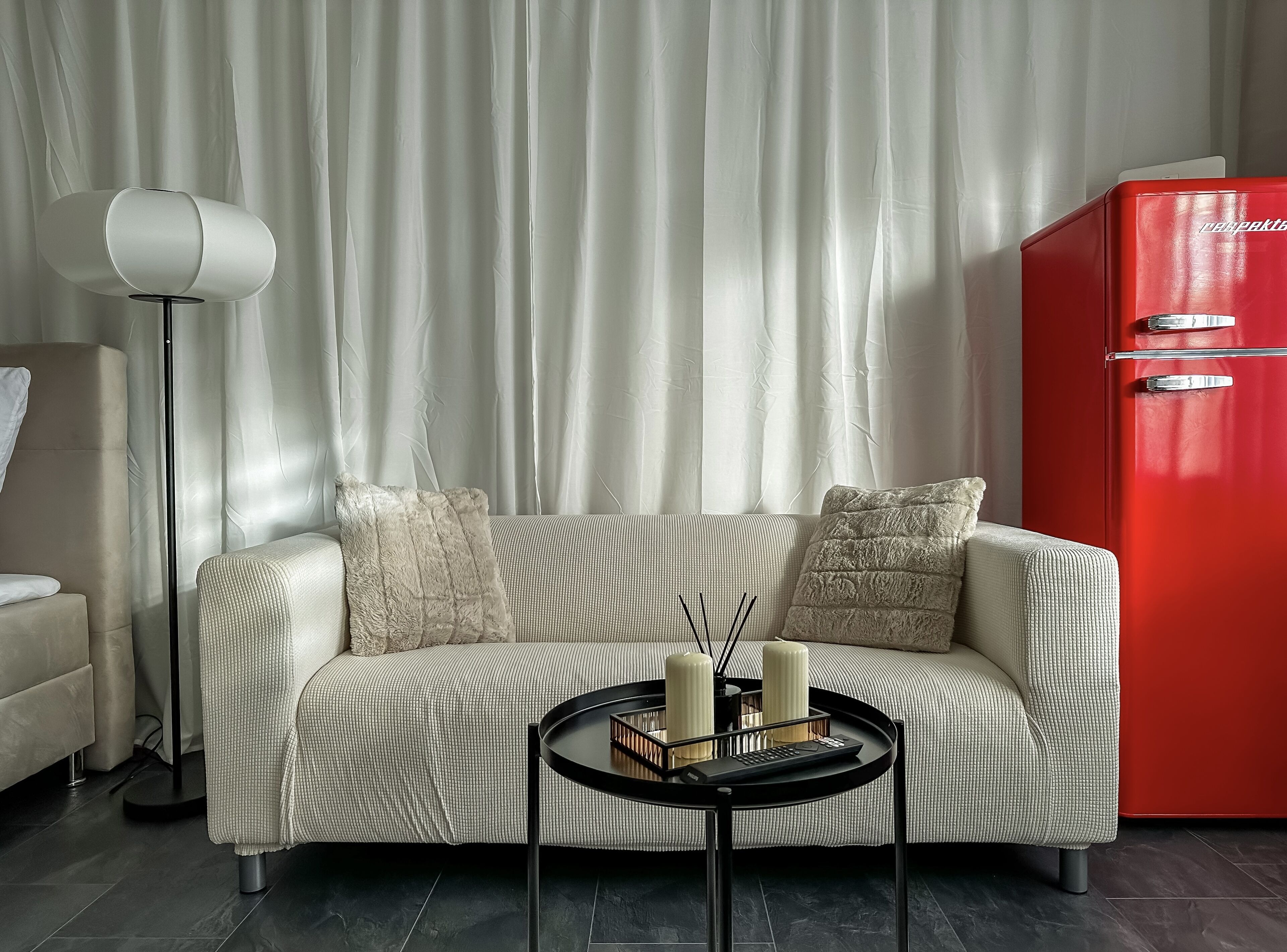 Ein modernes Wohnzimmer mit einer Couch, einem Couchtisch mit Kerzen, einer Stehlampe und einem roten Gerät.