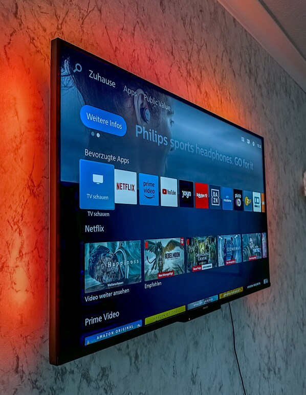 A flat-screen TV mounted on a textured wall displaying a digital interface with app icons and content thumbnails.