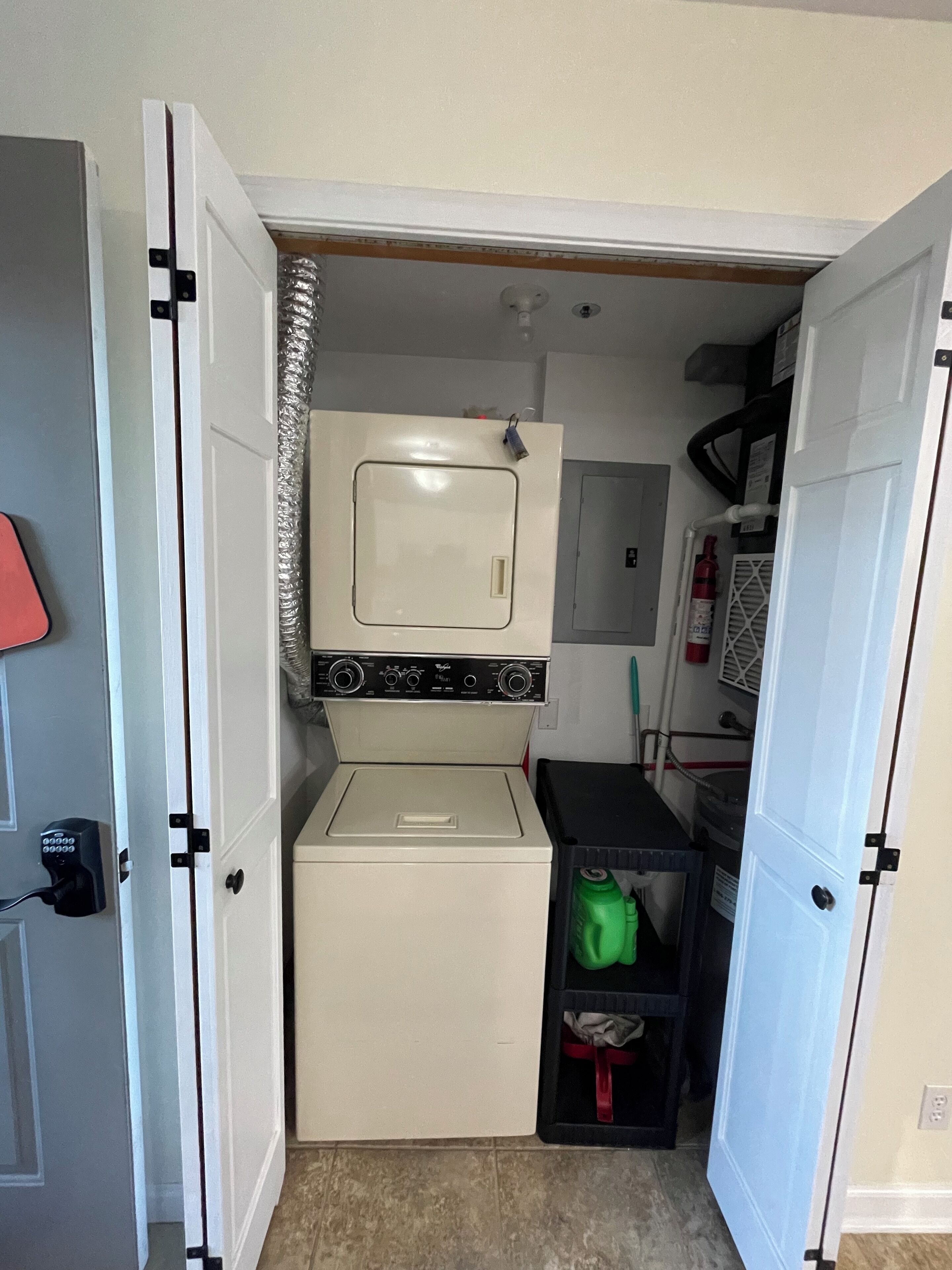 A compact laundry room with a washer and dryer, a small shelf with a green bottle, and a fire extinguisher.