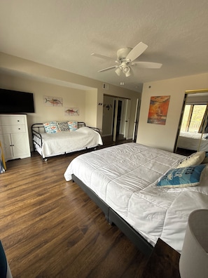 A bedroom with two beds, a ceiling fan, wooden flooring, and a wardrobe.