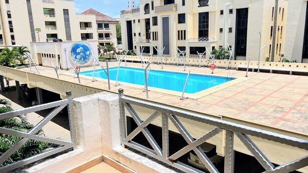 A swimming pool with a metal railing, surrounded by buildings with balconies and a clear sky. - Lux Suites Marrakech Apartments (Mombasa)