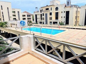 A swimming pool with a metal railing, surrounded by buildings with balconies and a clear sky. - Lux Suites Marrakech Apartments (Mombasa)