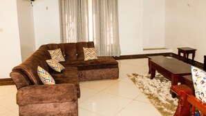 A living room with a brown sofa set, patterned cushions, a wooden coffee table, and a patterned rug. - Lux Suites Marrakech Apartments (Mombasa)