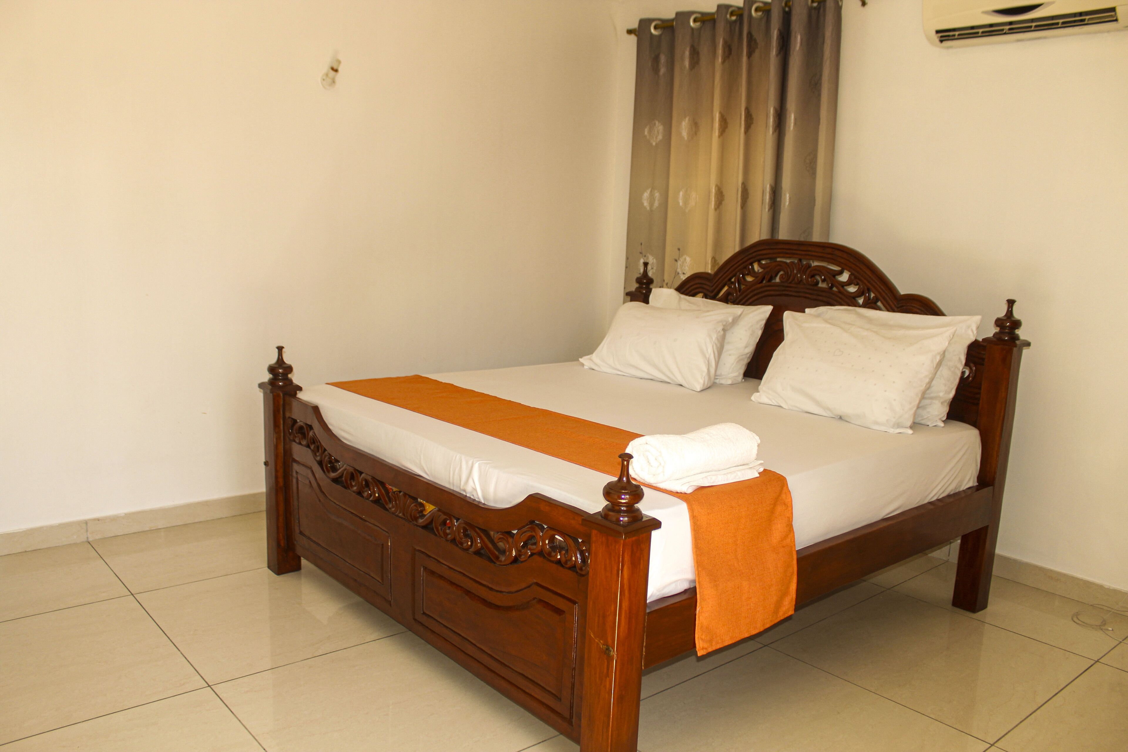 A wooden bed with a white and orange bedspread, a wooden headboard, and a white pillow.