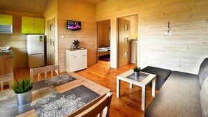 A compact wooden cabin with a kitchen, dining area, and a living room with a sofa and a TV. - Holiday homes with air conditioning, pool, jacuzzi (Jaroslawiec)