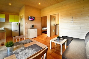 A compact wooden cabin with a kitchen, dining area, and a living room with a sofa and a TV. - Holiday homes with air conditioning, pool, jacuzzi (Jaroslawiec)