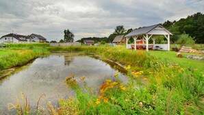 A rural landscape with a pond, grassy areas, and a wooden structure with benches. - Holiday homes with air conditioning, pool, jacuzzi (Jaroslawiec)