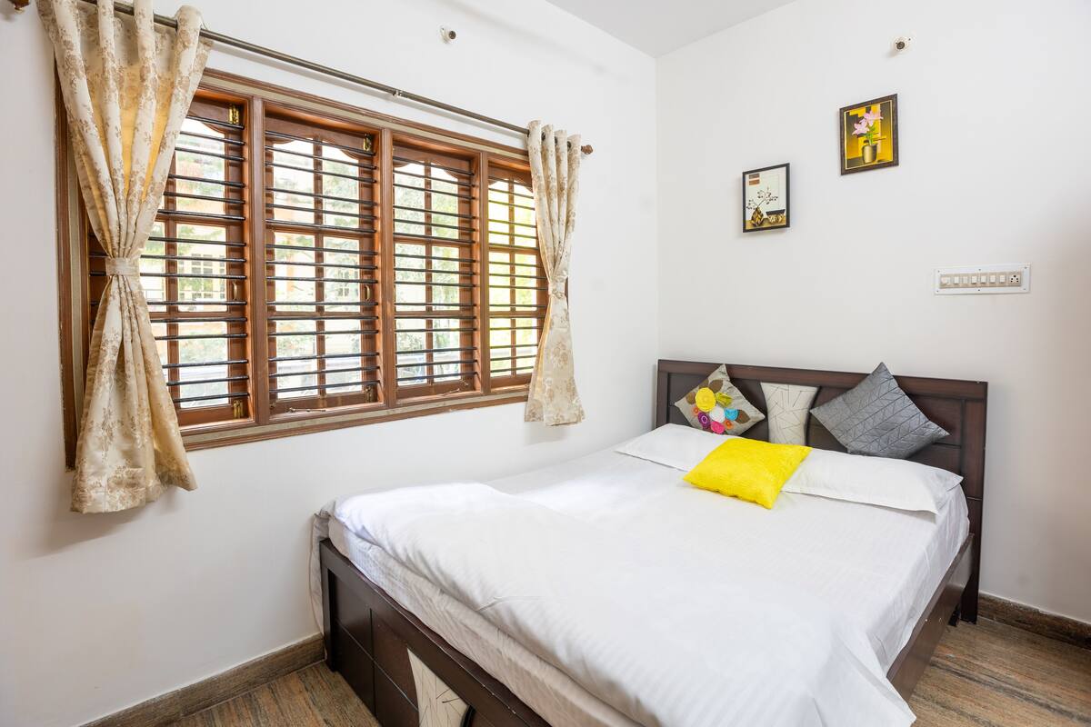 A bedroom with a bed, curtains, a window, and wall-mounted artwork.