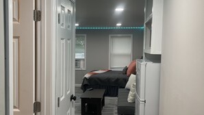 Un pasillo estrecho con una cama, un escritorio y un refrigerador.