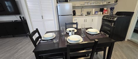 Une cuisine compacte équipée d’un four à micro-ondes, d’une cuisinière et d’un réfrigérateur. On y trouve une table à manger, mise avec des assiettes, des verres et des couverts.