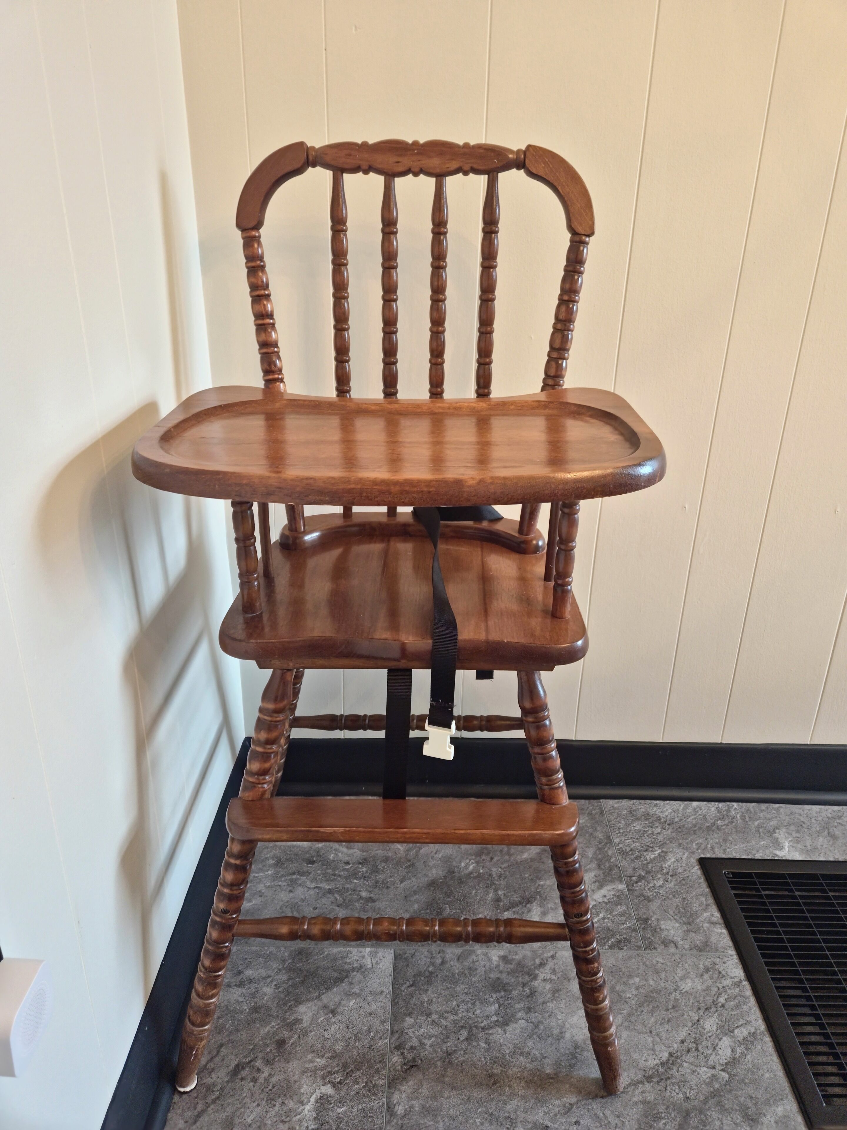 Una silla de madera con respaldo curvo y asiento plano, ubicada frente a una pared con piso de baldosas.