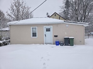 A single-story house with a white door and window, surrounded by snow. - Cozy home on a quiet street minutes to downtown Kingston! (Kingston)
