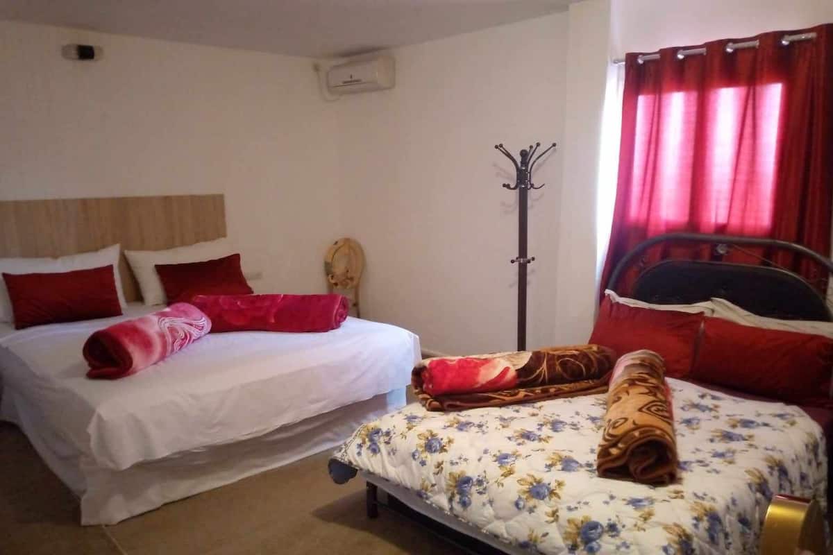 A bedroom with two beds, each with red and white bedding. There is a coat rack and a window with red curtains.