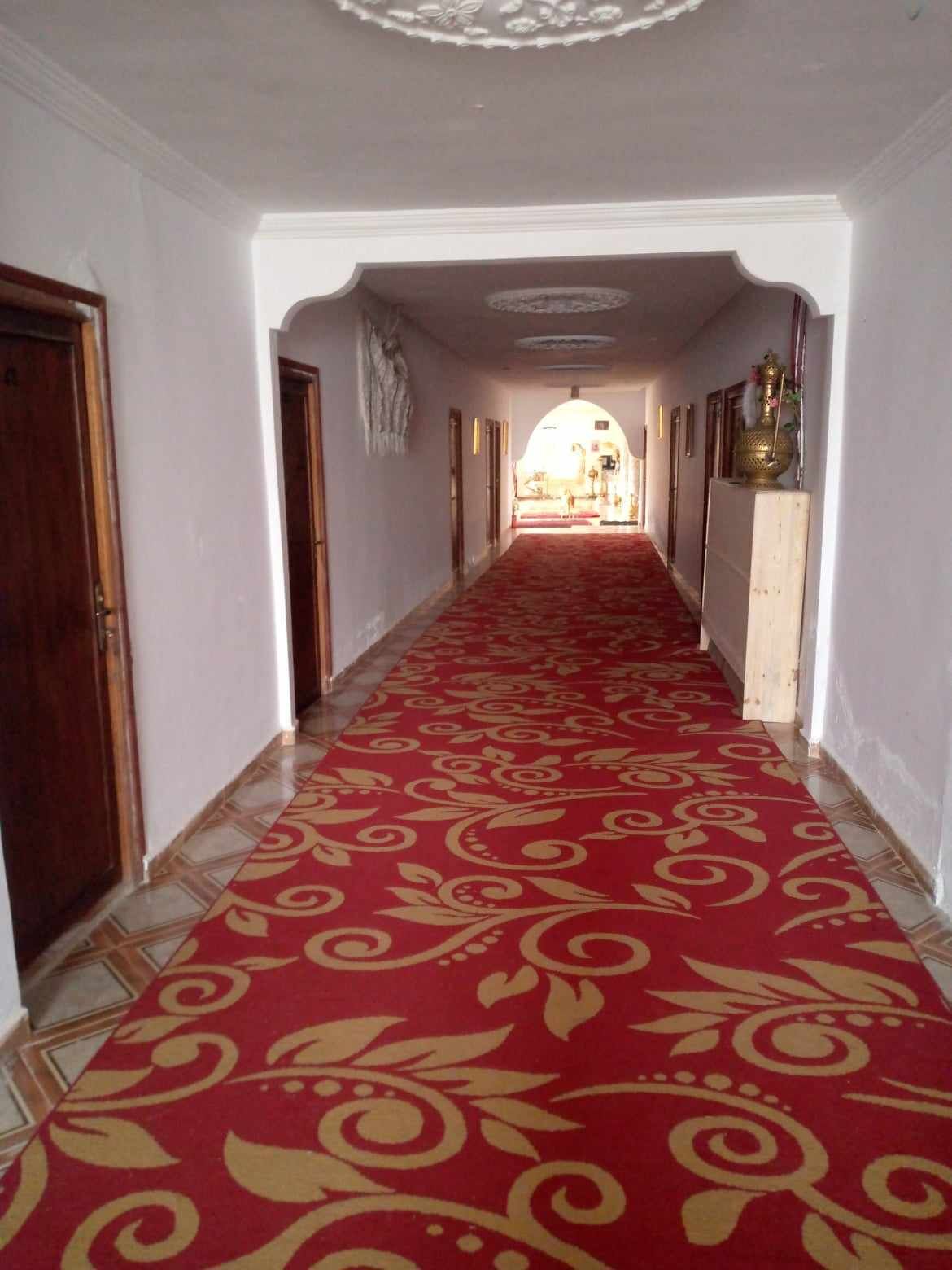 Un pasillo con alfombra roja, paredes blancas y puertas de madera.
