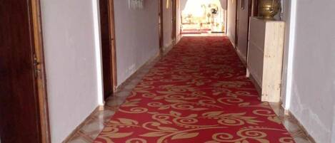 Un pasillo con alfombra roja, paredes blancas y puertas de madera.