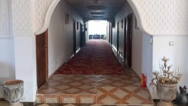A hallway with a checkered floor, an arched doorway, and a red carpet. - Hôtel et Restaurant Kinan (Amersid)