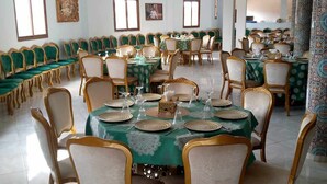 A spacious dining hall with multiple round tables, each set with green tablecloths and gold-rimmed chairs. - Hôtel et Restaurant Kinan (Amersid)