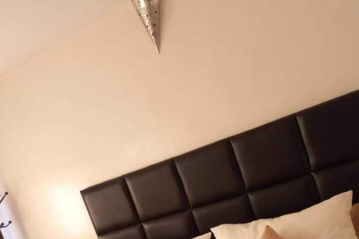 A hotel room with a large bed, a dark headboard, and multiple pillows.