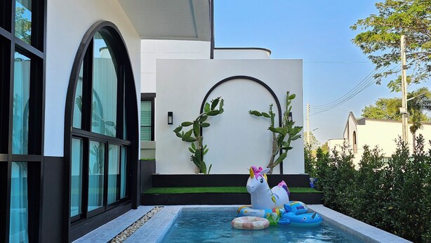 A swimming pool with a modern design, a white wall with a circular cutout, and a cactus plant. - Live with passion pool villa (Pak Chong)