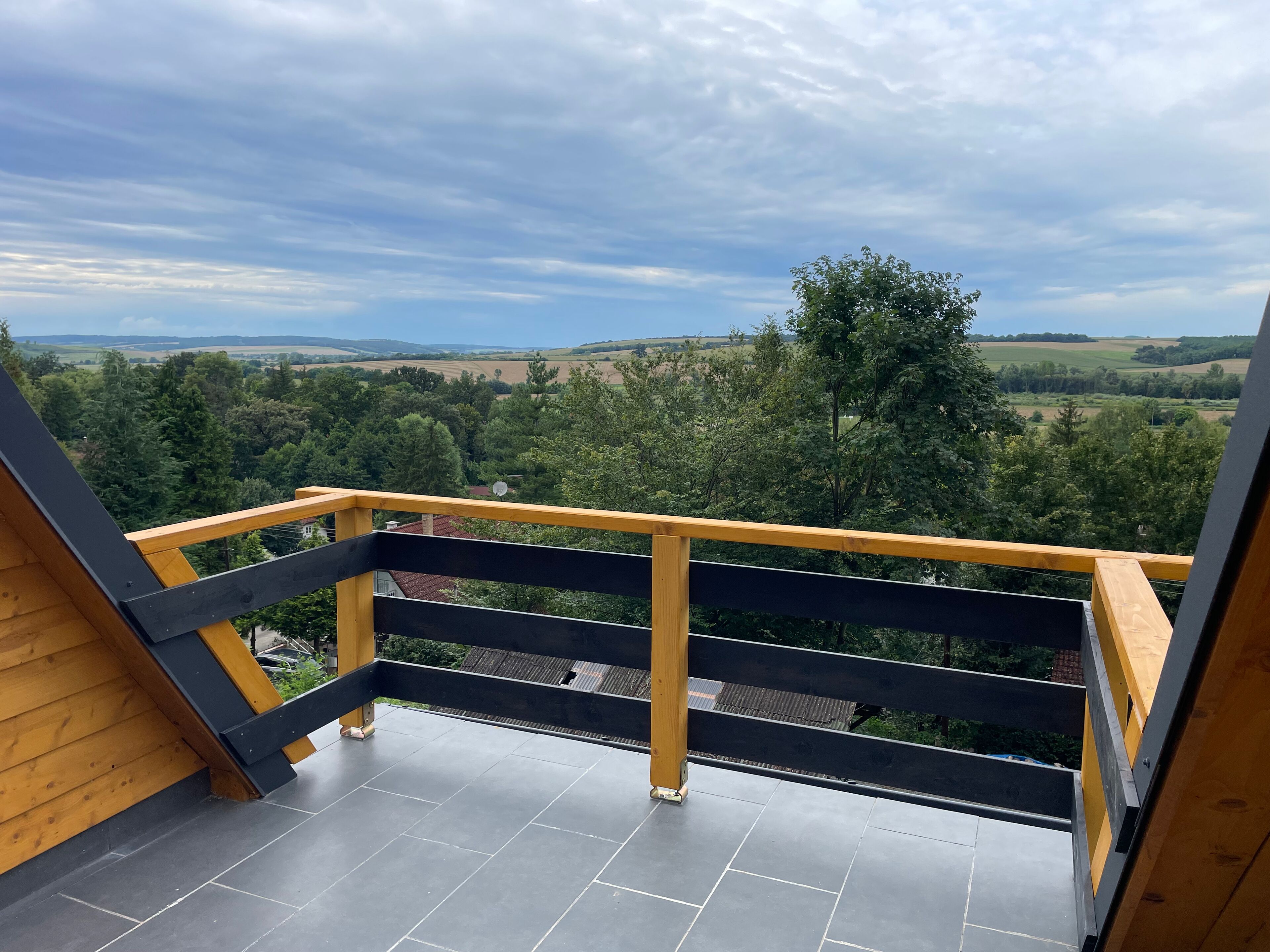 Een balkon met uitzicht op een landelijk landschap, met een houten leuning en betegelde vloer.