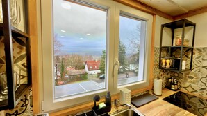 A kitchen with two large windows, a wooden countertop, and a shelf with kitchen items. - Calm Resort Hertelend (Magyarhertelend)