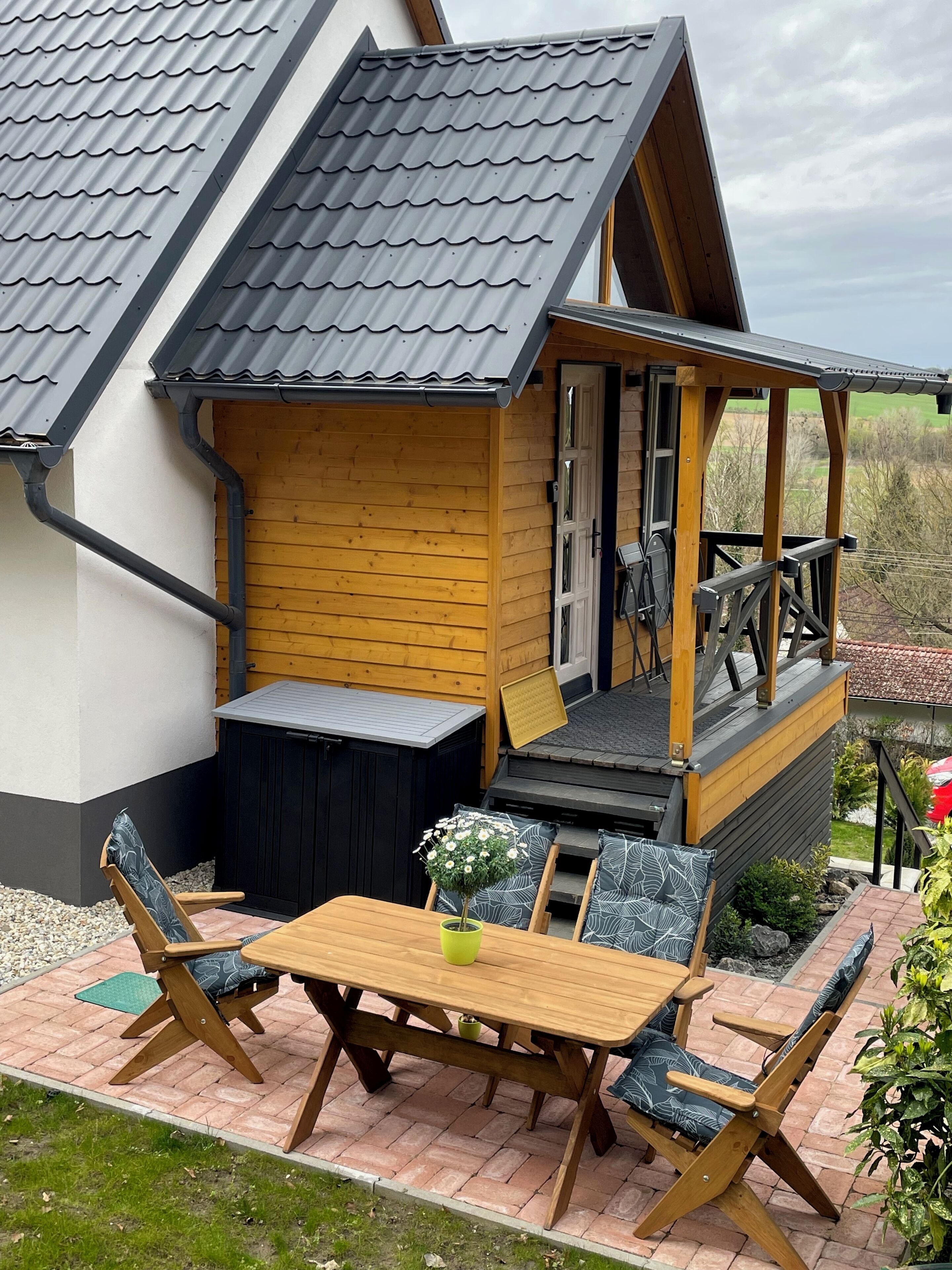 A wooden deck with a table and chairs, a small wooden structure with a balcony, and a garden area with plants.