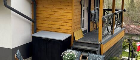 A wooden deck with a table and chairs, a small wooden structure with a balcony, and a garden area with plants.