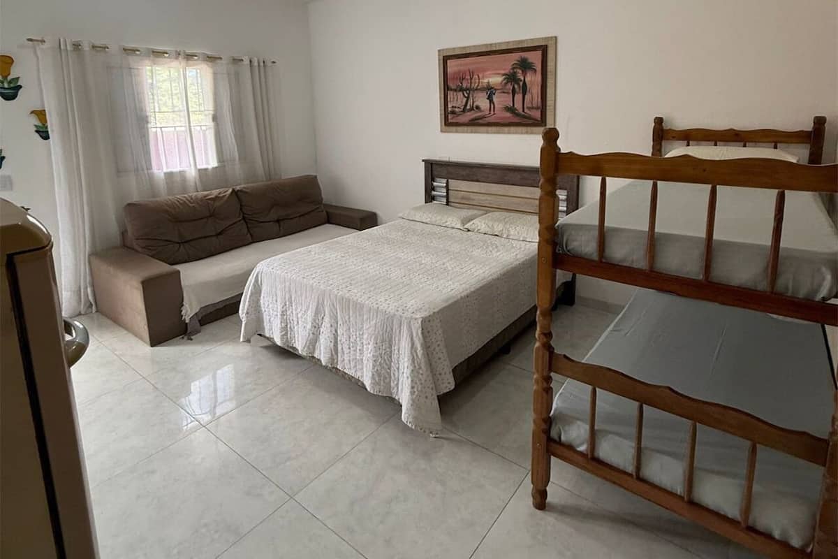A bedroom with a bed, a wooden bunk bed, a sofa, and a painting on the wall.