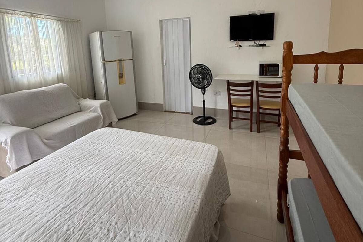 A hotel room with a bed, a sofa, a desk with a chair, a television, and a refrigerator.
