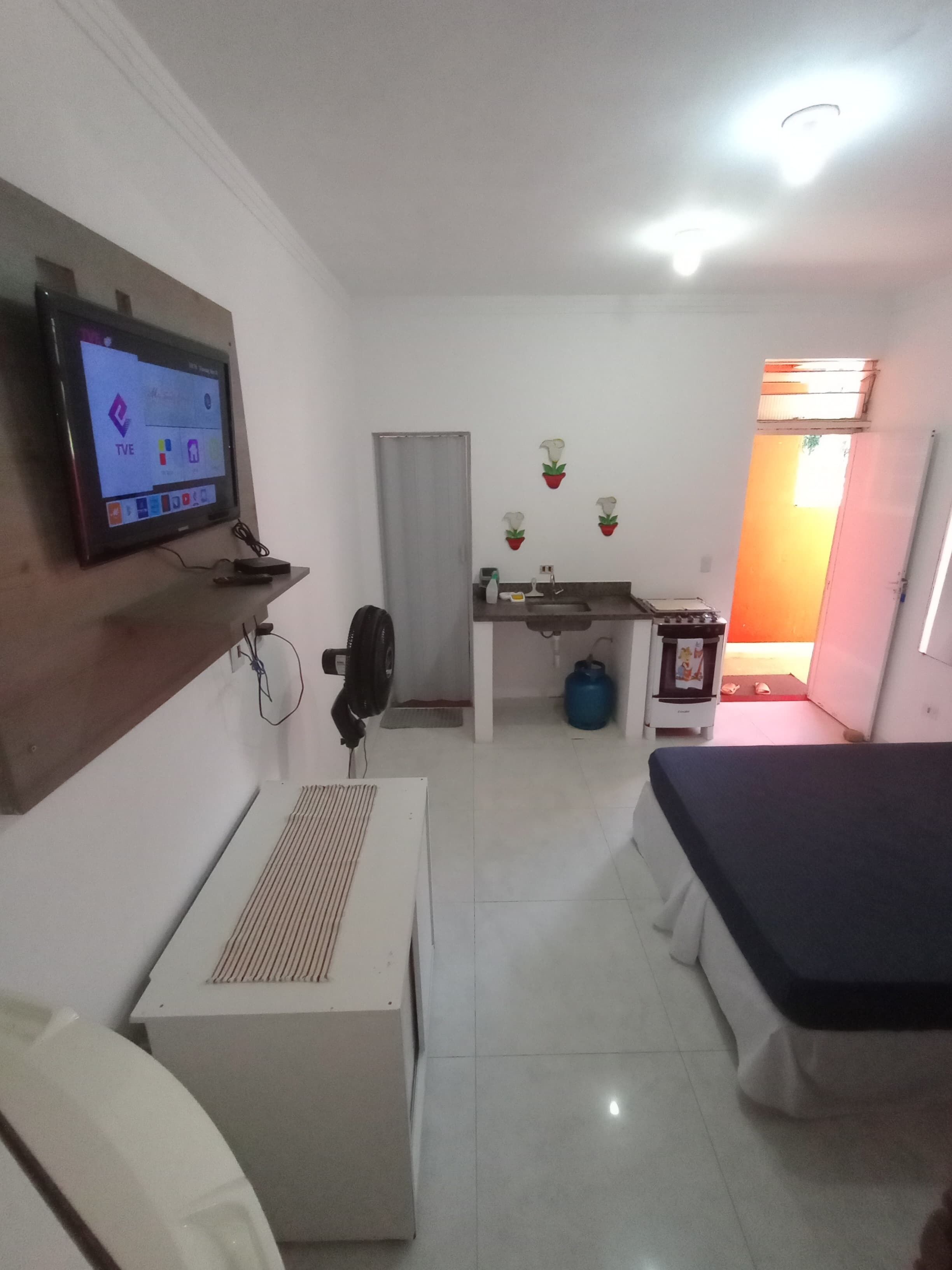 Een kamer met een aan de muur bevestigde televisie, een bed, een kleine tafel en een kitchenette.