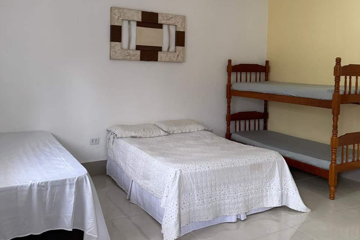A room with two single beds, a wooden bunk bed, and a wall-mounted artwork.