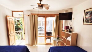 Quarto de hotel com duas camas, ventoinha no teto, televisão e vista para o exterior.