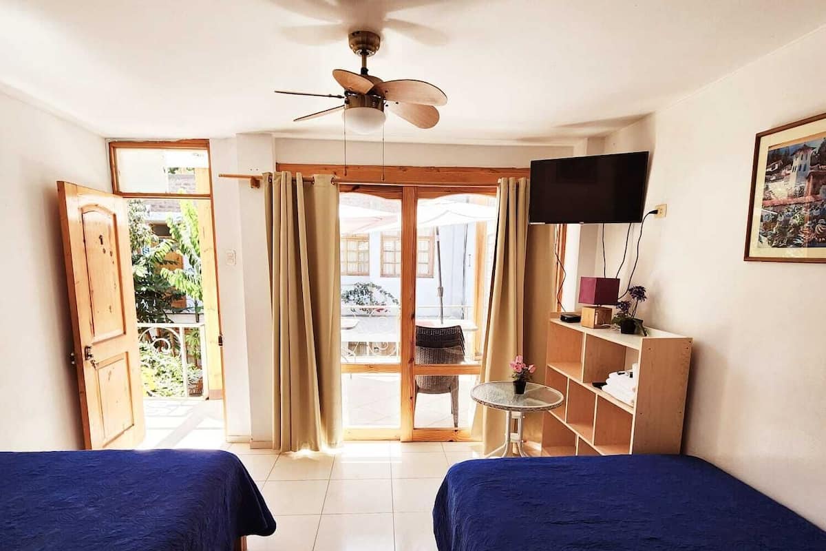 Habitación de hotel con dos camas, ventilador de techo, televisión y vista al exterior.