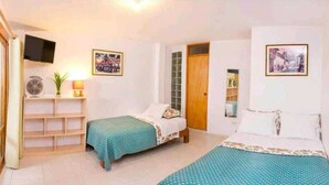 Um quarto com duas camas, uma estante com abajur e uma TV na parede.