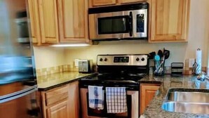 Una cocina con armarios de madera, electrodomésticos de acero inoxidable, encimeras de granito y salpicadero de azulejos.
