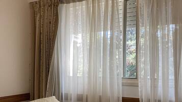 Un dormitorio con cama, ventana con cortinas translúcidas y unidad de aire acondicionado en la pared.