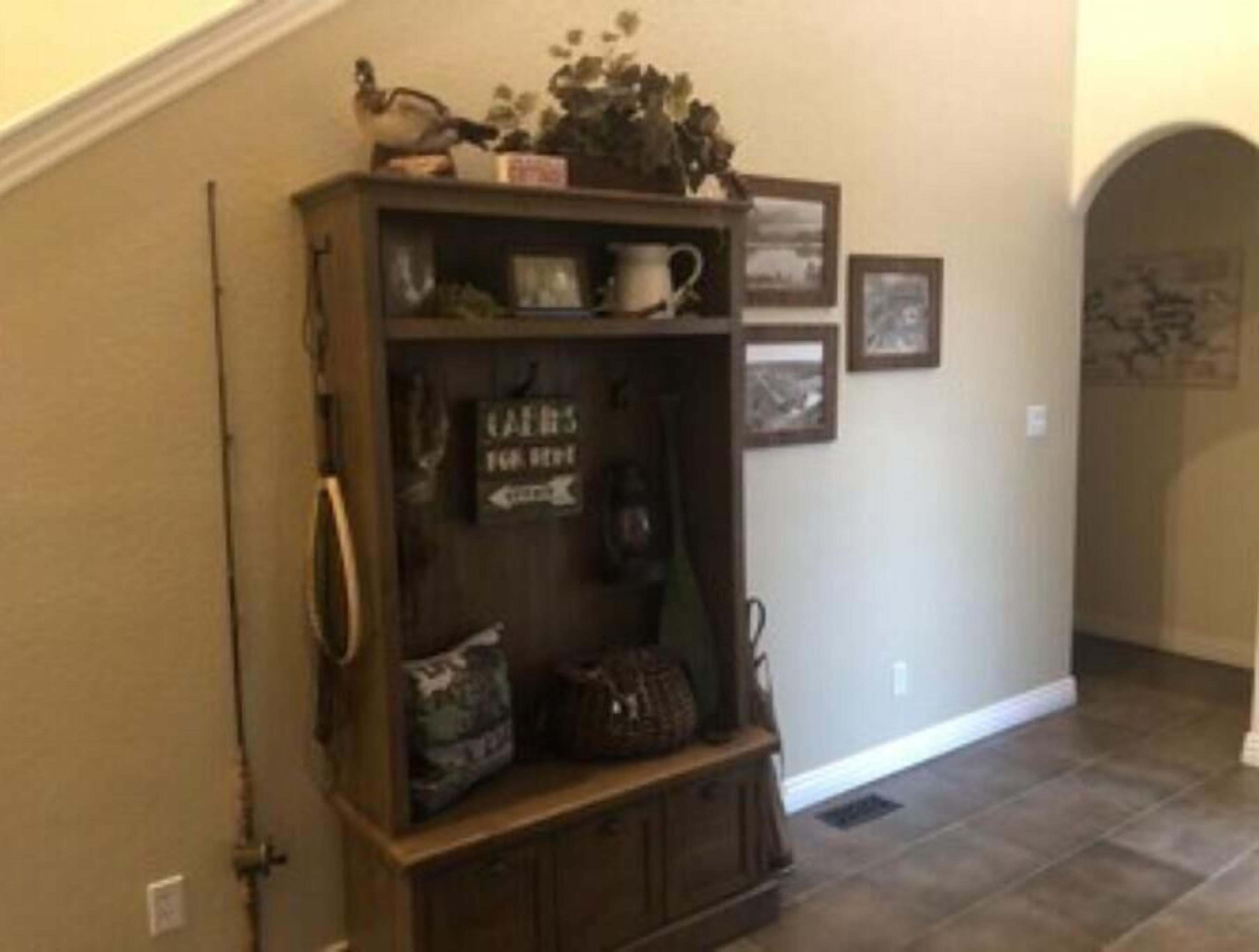 A wooden cabinet with a sign that reads "CAKES FOR SALE" in a hallway with tiled flooring and framed pictures on the wall.