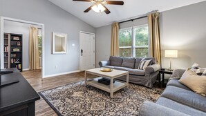 A living room with a ceiling fan, a sofa, a coffee table, a bookshelf, and a window with curtains.