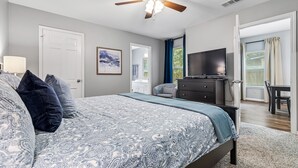 A bedroom with a bed, a ceiling fan, a TV, a desk, and a chair.