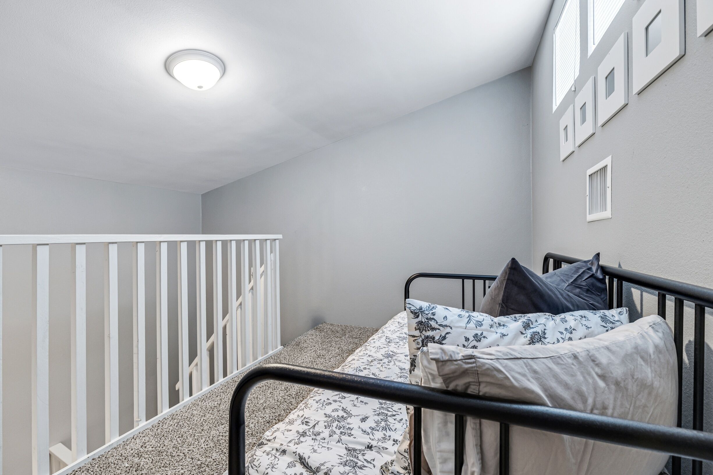 Une chambre à coucher avec un lit, une balustrade blanche, un luminaire au plafond et une fenêtre avec des volets.
