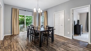 A dining area with a dark wooden table and chairs, a chandelier, and a view of a garden through large windows.