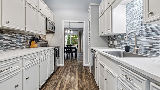 A modern kitchen with white cabinetry, a tiled backsplash, and a wooden floor.