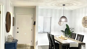 A dining area with a wooden table, chairs, and a hanging light fixture. - Cozy, spacious seaside condo in Ocean Village! (Fort Pierce)
