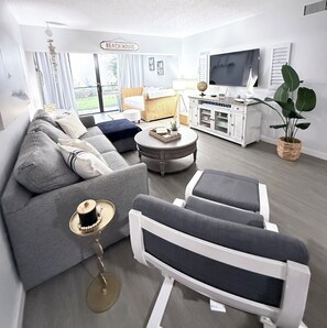 Uma sala de estar moderna com sofá, poltronas, mesa de centro, televisão e estante de livros.