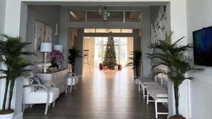 A spacious lobby with a high ceiling, a central Christmas tree, and a modern design with white furniture and potted plants. - Cozy, spacious seaside condo in Ocean Village! (Fort Pierce)