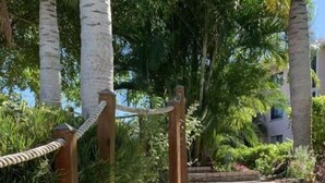 A stone staircase with a wooden handrail, surrounded by lush greenery and palm trees. - Cozy, spacious seaside condo in Ocean Village! (Fort Pierce)