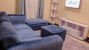 Una sala de estar moderna con un sofá modular, un televisor de pantalla plana, un mueble de entretenimiento blanco y una planta en maceta.