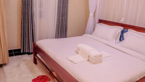 Una cama bien hecha con sábanas blancas y una almohada azul, un cabecero de madera y un par de pantuflas rojas sobre una alfombra blanca.